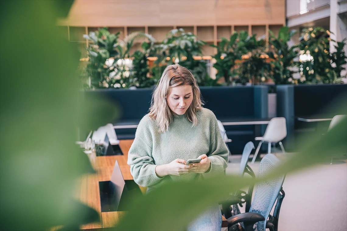 vrouw in kantoorruimte kijkend naar telefoon in haar handen